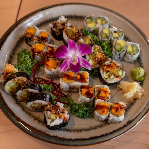 Assorted sushi rolls with avocado, sweet potato, and other fillings, garnished with a purple orchid.