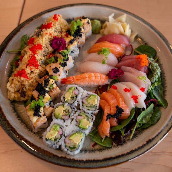 A large platter of diverse sushi, sashimi, and rolls, garnished with roe and edible flowers.