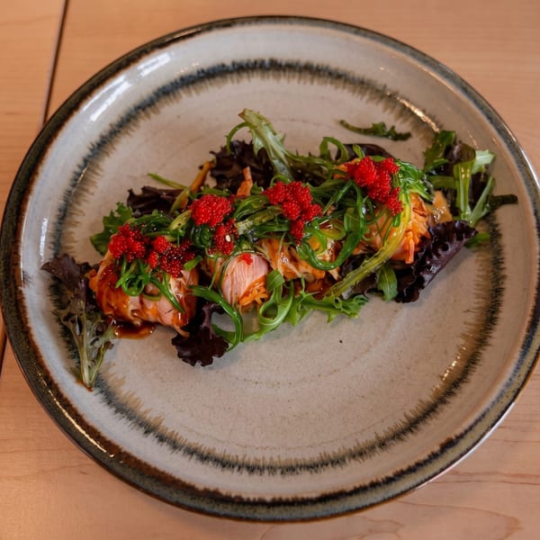 Salmon sashimi with seaweed salad, red tobiko, and sauce on a decorative plate.