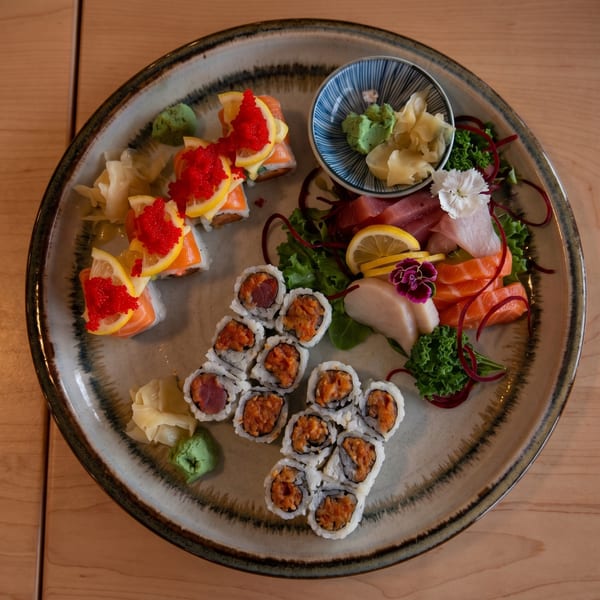 A large platter of sushi rolls, sashimi, wasabi, and pickled ginger on a wooden table.