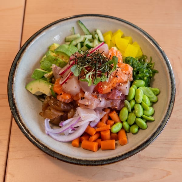 A colorful poke bowl with salmon, tuna, avocado, edamame, carrots, and seaweed salad.